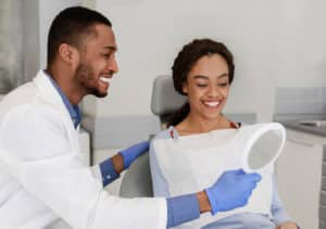 Friendly,Black,Dentist,Giving,Mirror,To,His,Happy,Female,Patient