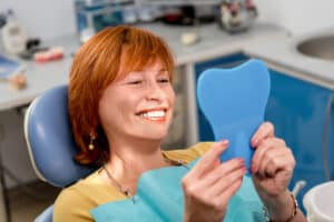 A woman looking in the mirror after getting All-on-4 implants in Houston, TX